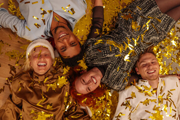 Four happy friends laying on the floor while gold confetti fall on them