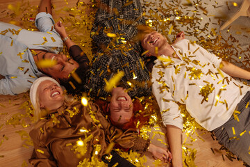 Four people laying on the floor while gold confetti fall on them