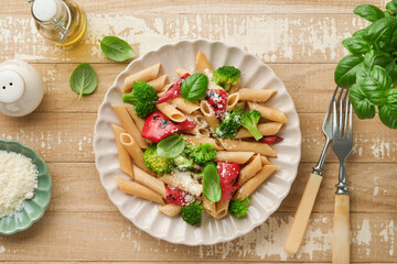 Wholegrain pasta penne with broccoli and red grilled bell pepper and on light wooden rustic background table. Vegan pasta. Traditional Italian cuisine. Flat lay. Copy space.