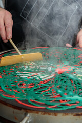 Preparation of colored pancakes. The cook's hands level the dough on the baking surface. Close-up