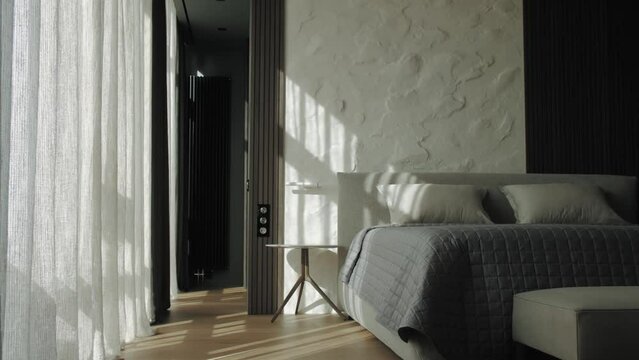 Dolly shot of front view of bedroom, sun rays trough the window in large bedroom on the pillow on the bed, bedding, gray blanket slow motion.
