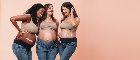 Happy multicultural mothers celebrating the third trimester of pregnancy in a studio - obrazy, fototapety, plakaty