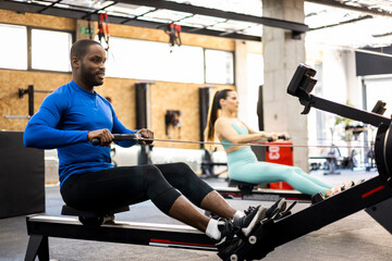 A couple of athletes of different ethnicities are working their bodies with a magnetic air rowing...