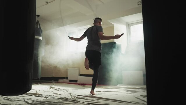 Sportsman jumps on rope in combat gym. Strong boxer does exercises with skip rope in martial arts club slow motion. Leg muscles training techniques
