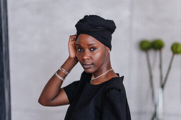 Portrait of an elegant African girl in a black turban in a black dress looking at the camera...