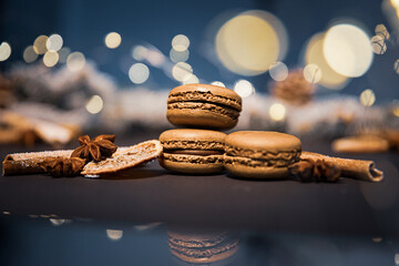 Chocolate macarons cookies among pieces of dried orange on a dark background with soft light from...