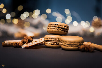Chocolate macarons cookies among pieces of dried orange on a dark background with soft light from...
