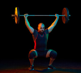 Strong, muscular, young athlete, bodybuilder doing squats and lifting barbell, heavy weights...