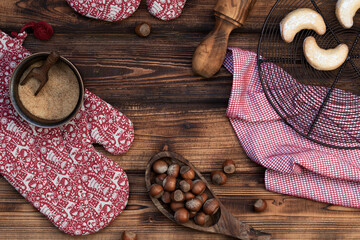 Christmas background. Homemade vanilla candy on a chilling grid, red Christmas mittens and kitchen towel on a wooden background with hazelnuts and a wooden dough roller.  Christmas banner. Top view.
