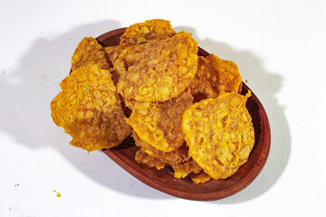 a pile of savory tempeh chips, served on a brown wooden plate with a plain white background