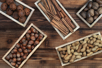 Various types of nuts, cinnamon and rusty bells on small teak trays on a natural wooden background. Top view. Natural banner. Autumn and Advent or Christmas background. 