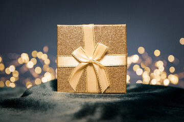 Gold gift with a bow on a dark background and on a glass table with soft lighting on a green...