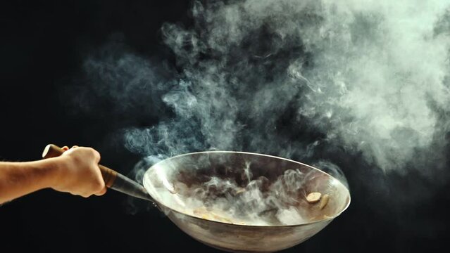 Man cooking delicious wok noodles, frying vegetables in wok pan, preparing ingredients against black background. Concept of Asian food, cuisine, restaurant, taste, cooking, recipe