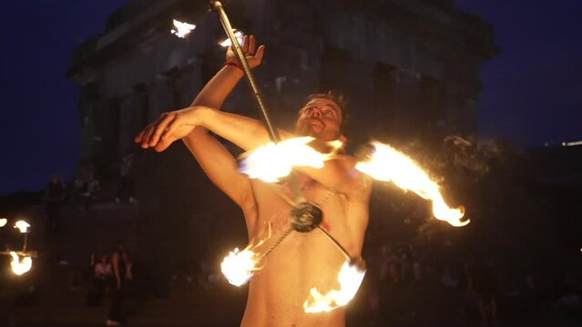 Fire show performance. Handsome male fire juggler performing with a burning contact dragon staff. Close-up. Slow motion