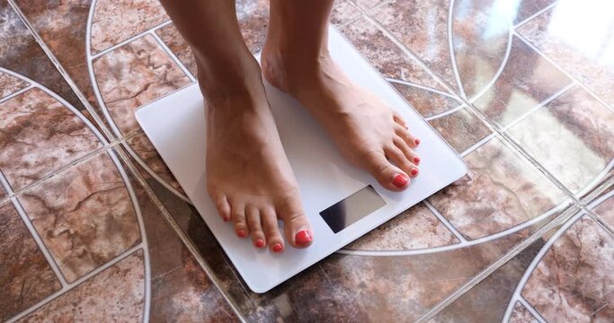 Woman measures weight on scales in morning. Overweight and measurement of body fat concept