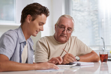 Elderly man helping grandson to manage personal finances and household expense