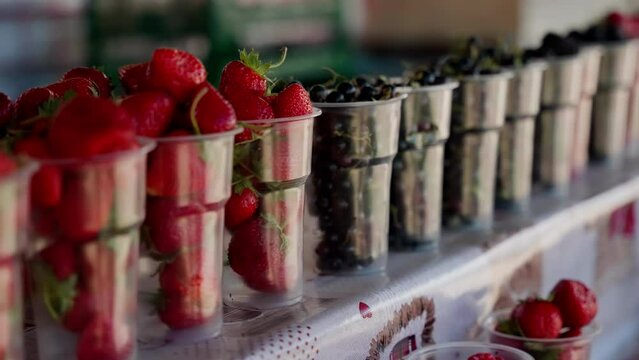 A row of plastic cups with strawberries and blueberries. Juicy bursts of red sweetness adorn a row of plastic cups, beckoning from an indoor store, enticing dessert lovers with luscious strawberries