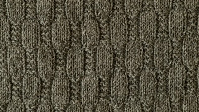 Video of fragment of gray knitted sweater with pattern. Background with knitted leaf shape, knitting pattern with cables. Top view, close-up. Handmade knitting wool or cotton fabric texture. 