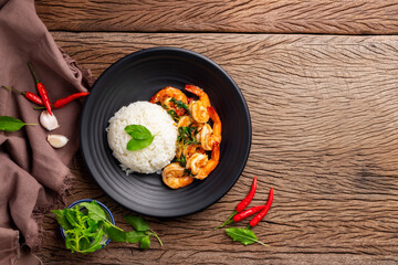 Stir-fried shrimp with basil Thai street food arranged on a black plate Spicy Thai food placed on a wooden table. Top view.