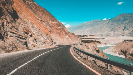 Road winds along a steep cliff face with barren mountains in the background and clear blue sky