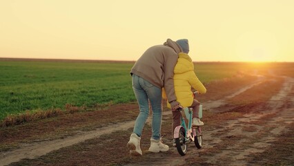 Mom teaches little girl to ride childrens bike on road in autumn. Happy family. Mother teaches his...