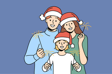 Christmas family of dad with mom and smiling child use sparklers celebrating new year holidays. Young parents and daughter in christmas santa hat wishing happy yuletide and xmas holiday