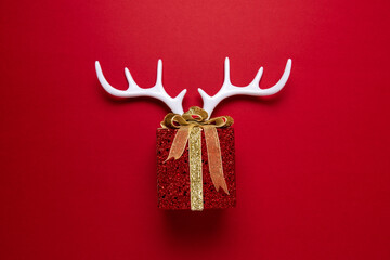 White reindeer antlers with gift box on red backdrop. Minimal New Year or Christmas background...