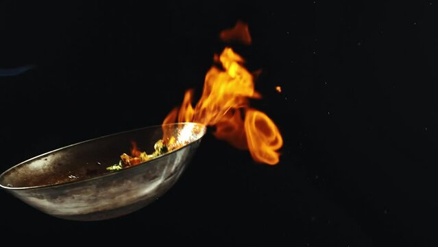 Chef cooking delicious wok noodles, frying vegetables and shrimps in pan with fire flames against black background. Concept of Asian food, cuisine, restaurant, taste, cooking, recipe