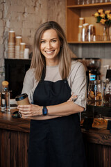A portrait of a poised female barista holding a takeaway coffee cup, standing in her modern cafe