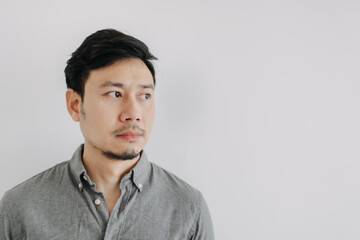 Close up of Asian man with beard wear grey t-shirt emotionless face, looking at empty space isolated over white background wall.