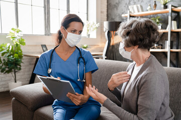 Coronavirus concept. Social distance. Nurse and elderly patient wearing protective masks talking about illness diseases, prescribing treatment and medication at home - obrazy, fototapety, plakaty