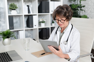 Elderly senior female doctor pediatrician general practitioner using digital tablet for consulting...