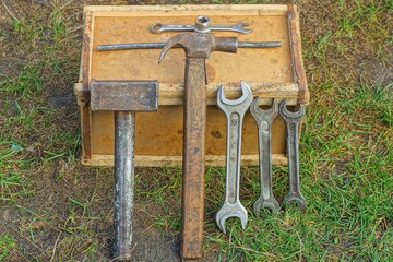 a lot of wrenches of various manual mechanical old iron wrenches of different sizes for plumbing repairs and two hammers  stand together near on a wooden box on the ground in the street 
