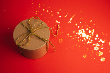 A gift box with a golden ribbon on a red background. Christmas gift, greeting background. Copy space, top view