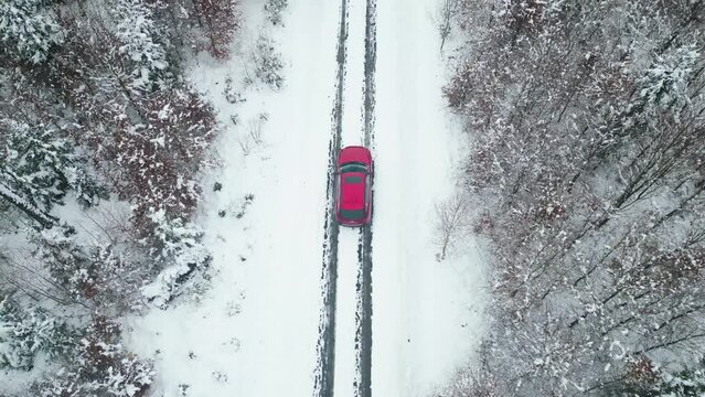 Top-down drone shot of a red car on a forest road in winter