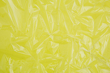 Crumpled texture of cling film on the bright lemon color paper