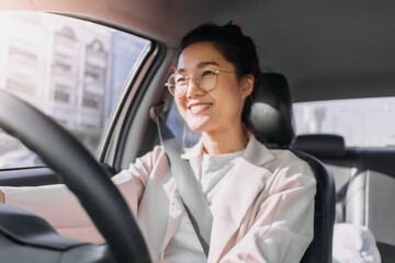 Front view of asian Thai woman wear eye glasses, happy smiling while driving a car alone on road, going to work in the morning.