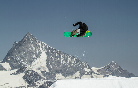 Anonymous man with snowboard jumping on snowy mountain against blue sky during vacation at Swiss Alps