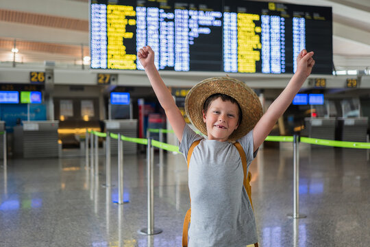 Portrait of happy cute boy in casuals and straw hat with missing teeth and outstretch arms smiling looking at camera and wearing backpack while waiting at airport terminal