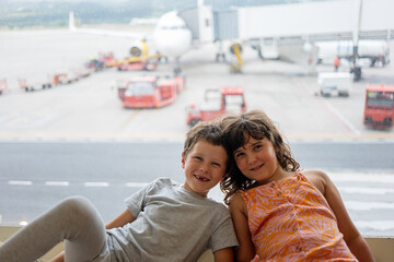 Happy siblings sitting against window at terminal