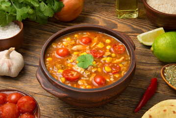 Easy Mexican chicken and rice soup in a terracotta soup bowl on a rustic wooden table with ingredients. - 685155919