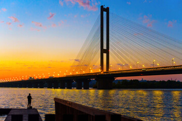 Naklejka premium Sunset Serenity: Cable-Stayed Bridge and Silhouetted Fisher