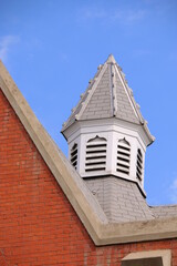 Obraz premium The white spire of a red brick building framed by the right angle of two lower walls and a clear blue sky.