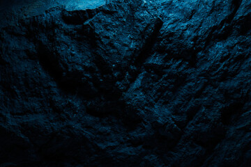 Black stone texture in blue neon lighting, dark abstract background. Natural mineral rock close up details, empty backdrop with copy space for design