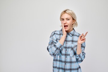 Young blond woman in casual pointing aside finger, demonstrating empty space for product or text...