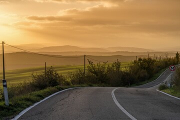 curvy and hilly country highway with power line and street sign at sunrise in the rolling hills of Tuscany