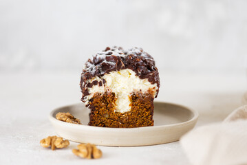 Dessert carrot cake with vanilla cream cheese, chocolate and walnuts on a light background.
