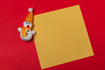 snowman and blank yellow sheet of paper on a red background, christmas concept