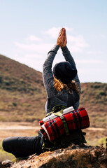 Back view of adventure woman doing yoga healthy position in front of a mountain in outdoor trekking...