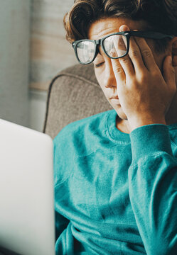Tired and stressed student at home using laptop on the sofa. Education and study concept leisure activity indoor. Young boy teenager worried in front of a notebook busy in online job. People and web
